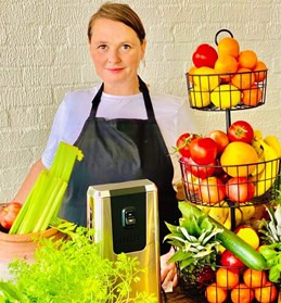 Woman in kitchen setting with fruit and veg in the foreground.